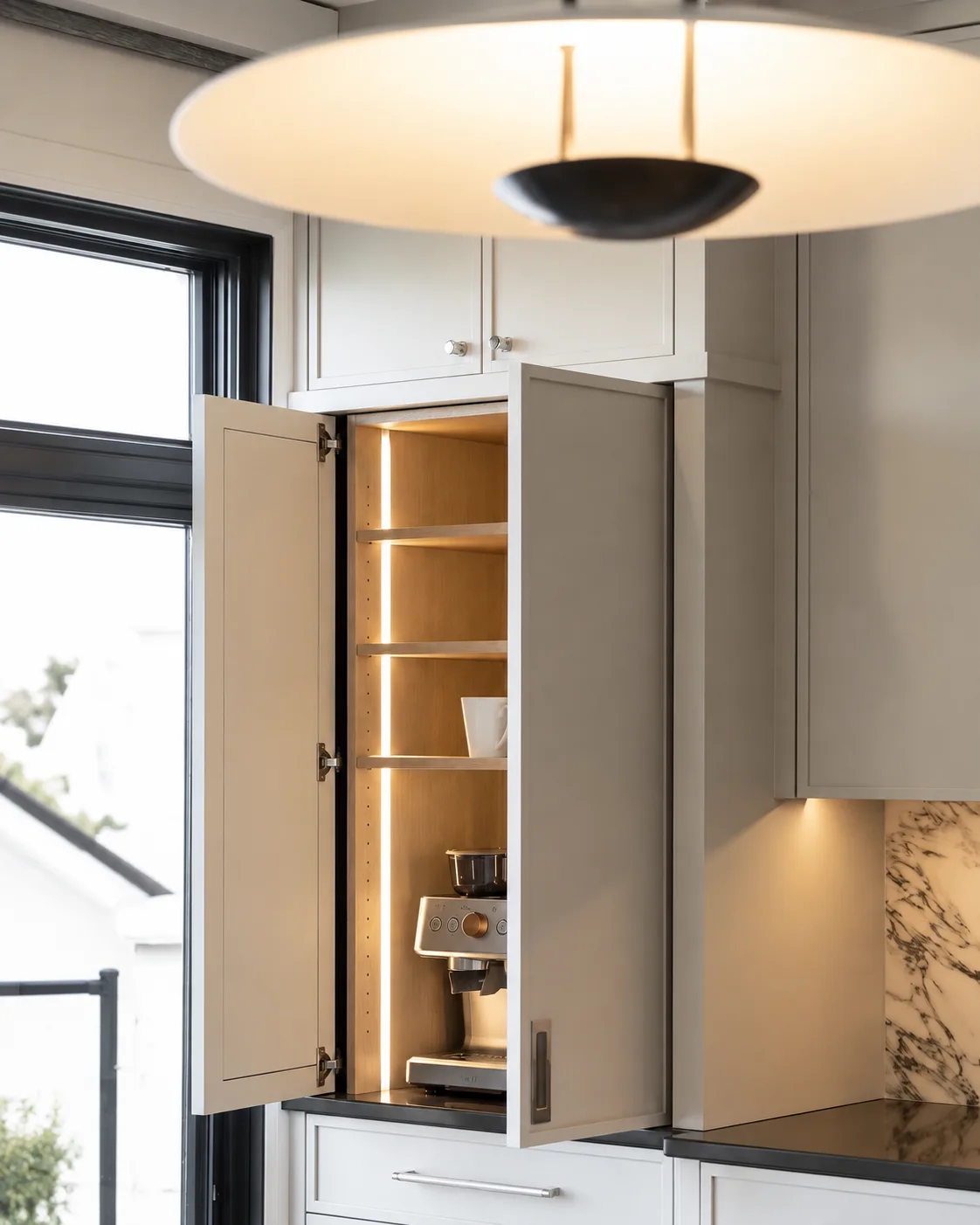 Detailed gray cabinetry with a warmly lit appliance garage and black window trim