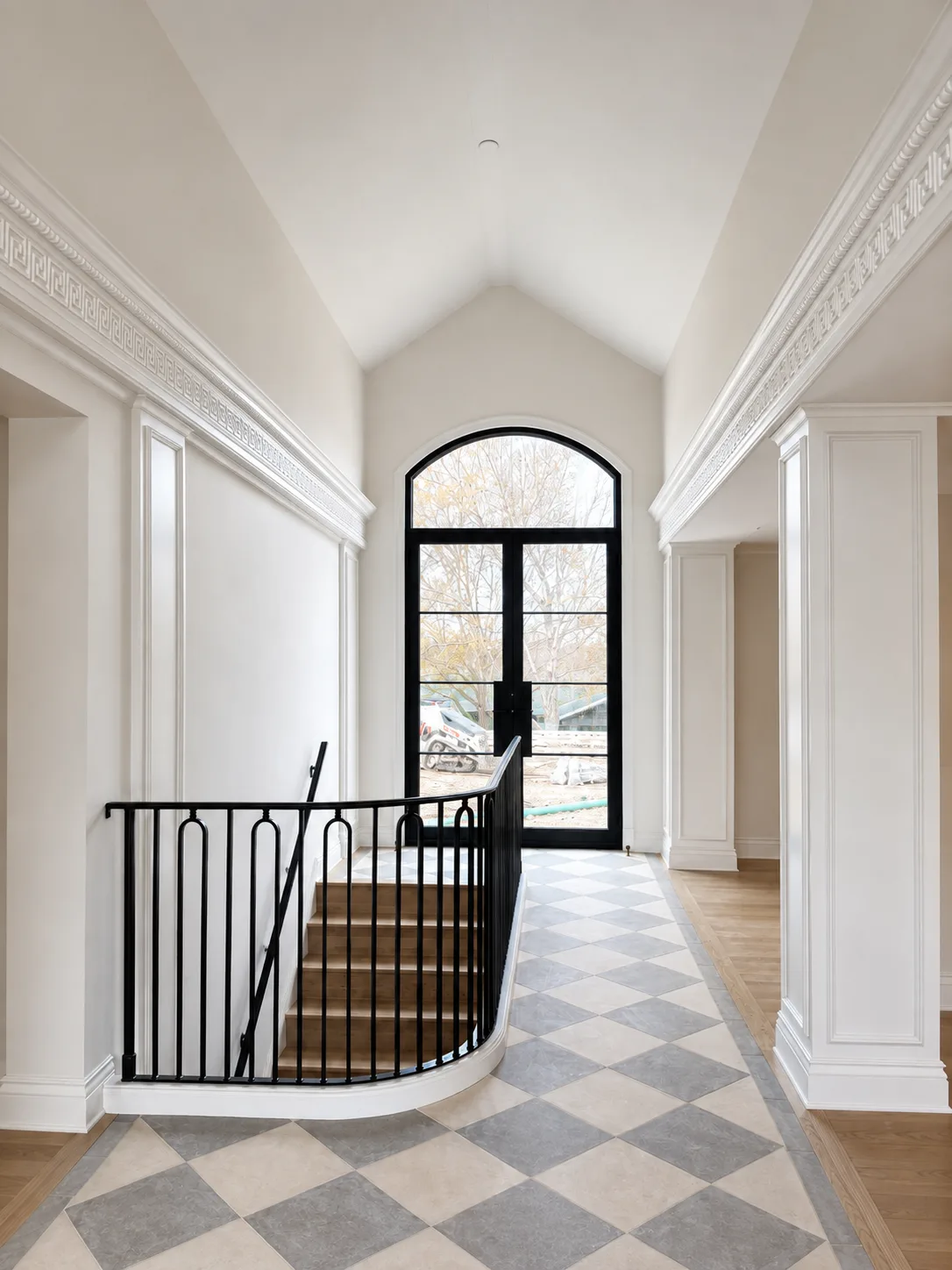 Bright entry hall with finished walls, detailed white millwork, black railings, and a checkerboard floor
