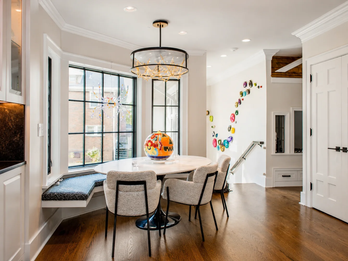 Bright breakfast room with white millwork, black windows, colorful art, and dark wood floors