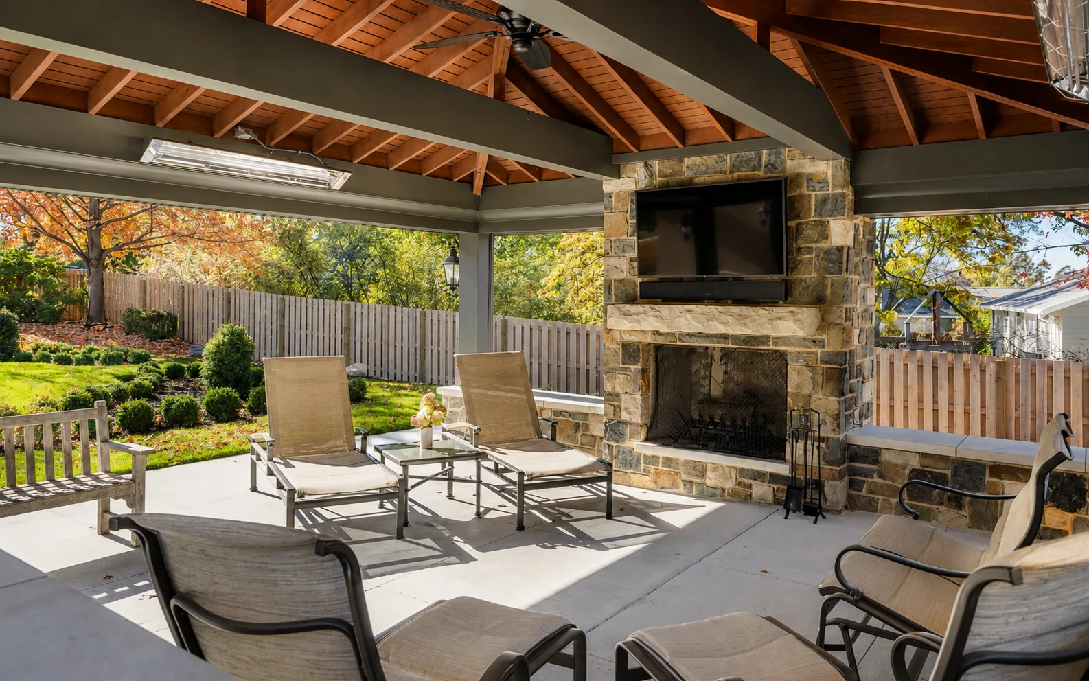 Covered outdoor pavilion with painted beams, a stained wood ceiling, and a stone fireplace