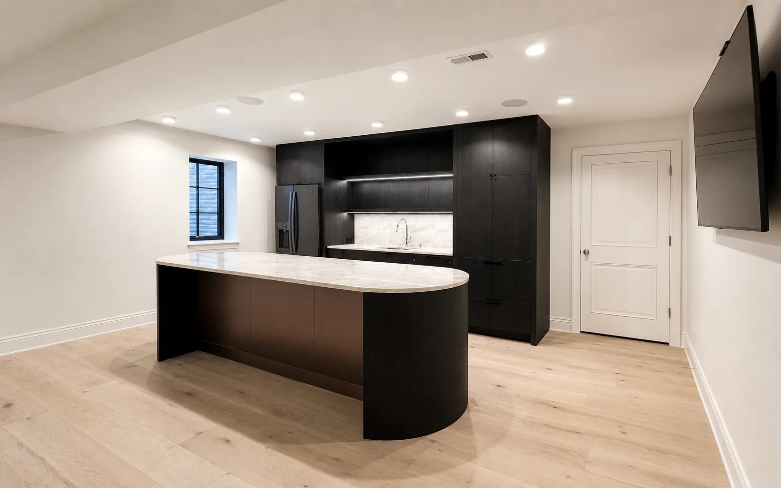 Lower-level kitchen with dark finished cabinetry, a curved island, white walls, and light wood floors