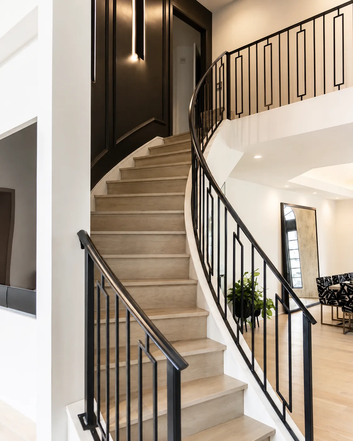 Curved staircase with a dark paneled accent wall, light wood steps, and black railings