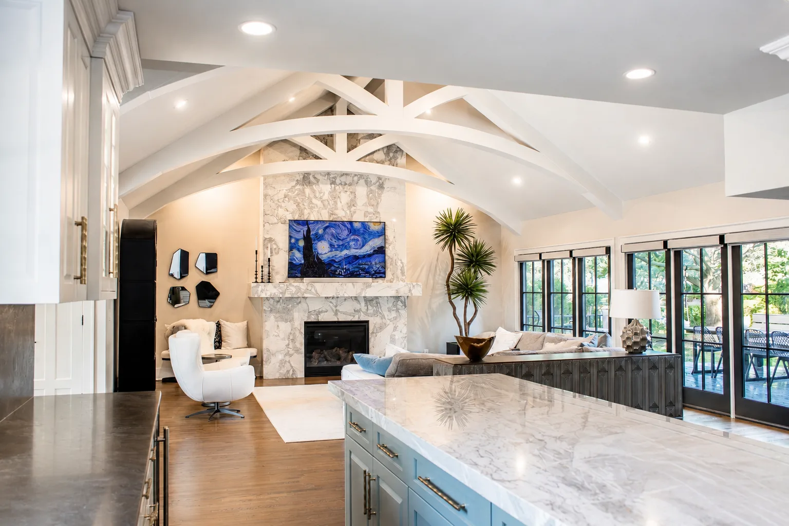 Bright open kitchen and great room with painted beams, cabinetry, and a light stone fireplace