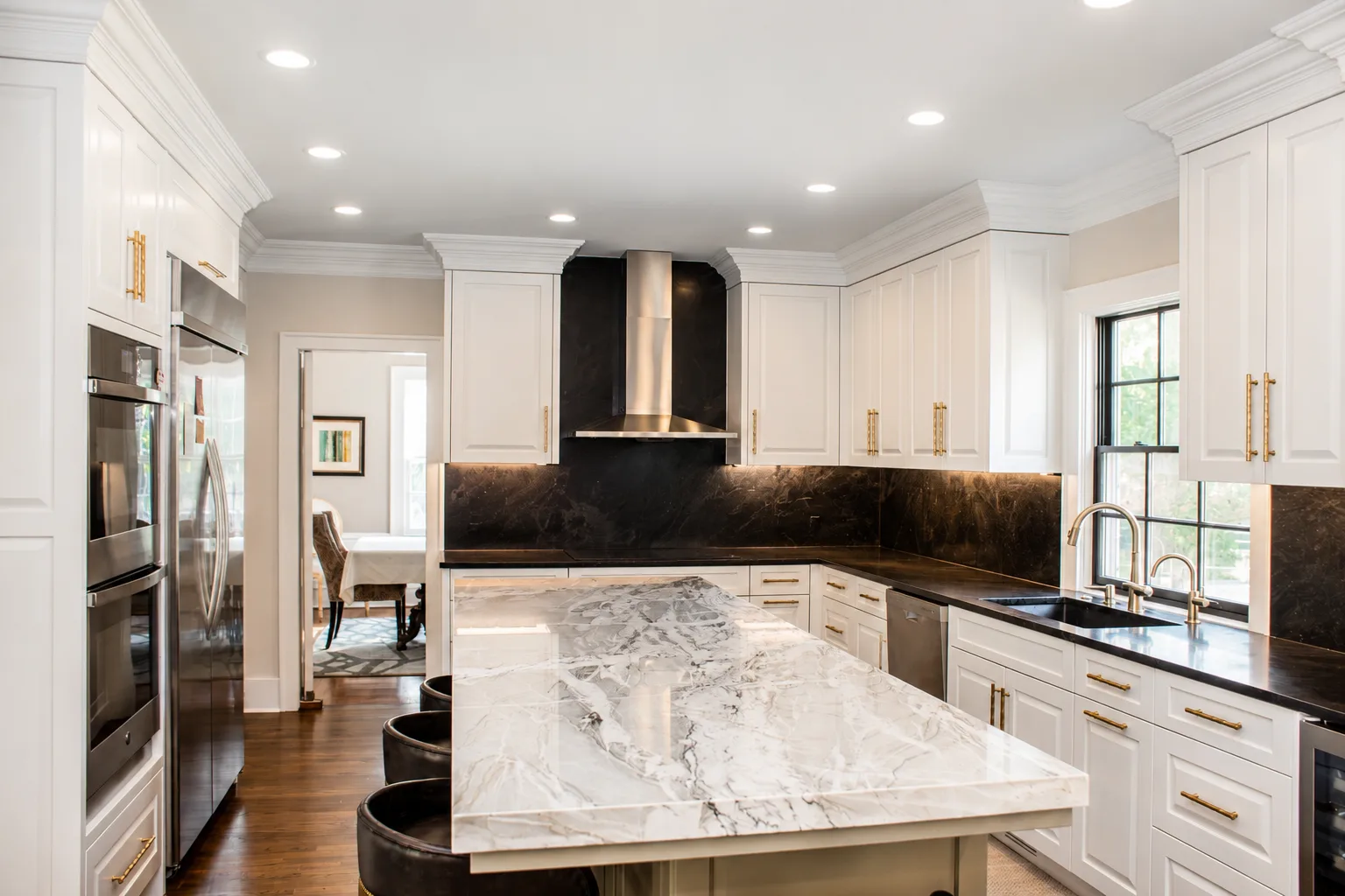 Bright white kitchen cabinetry with detailed crown molding, brass hardware, and dark stone accents