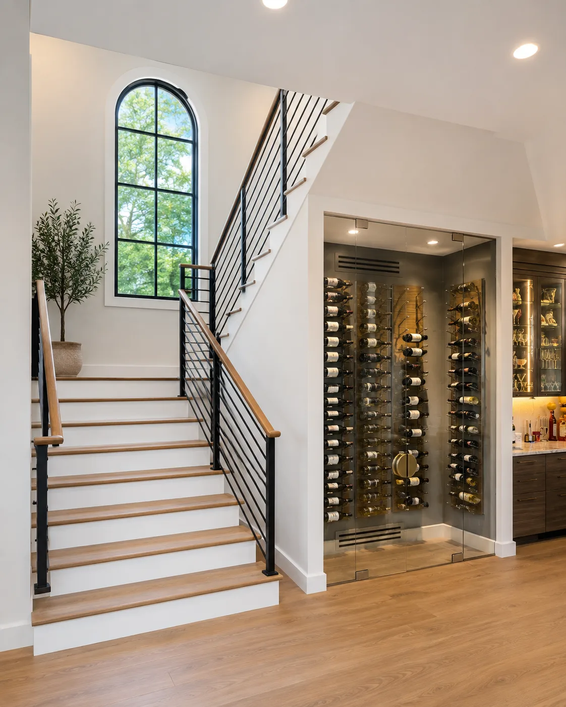 Modern stair hall with finished white walls, black railings, an arched window, and a glass wine room
