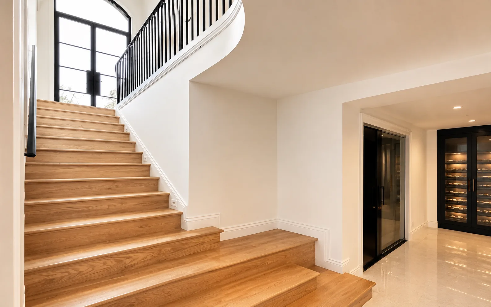 Broad light wood staircase with finished white walls, black railings, and a dark glass wine room