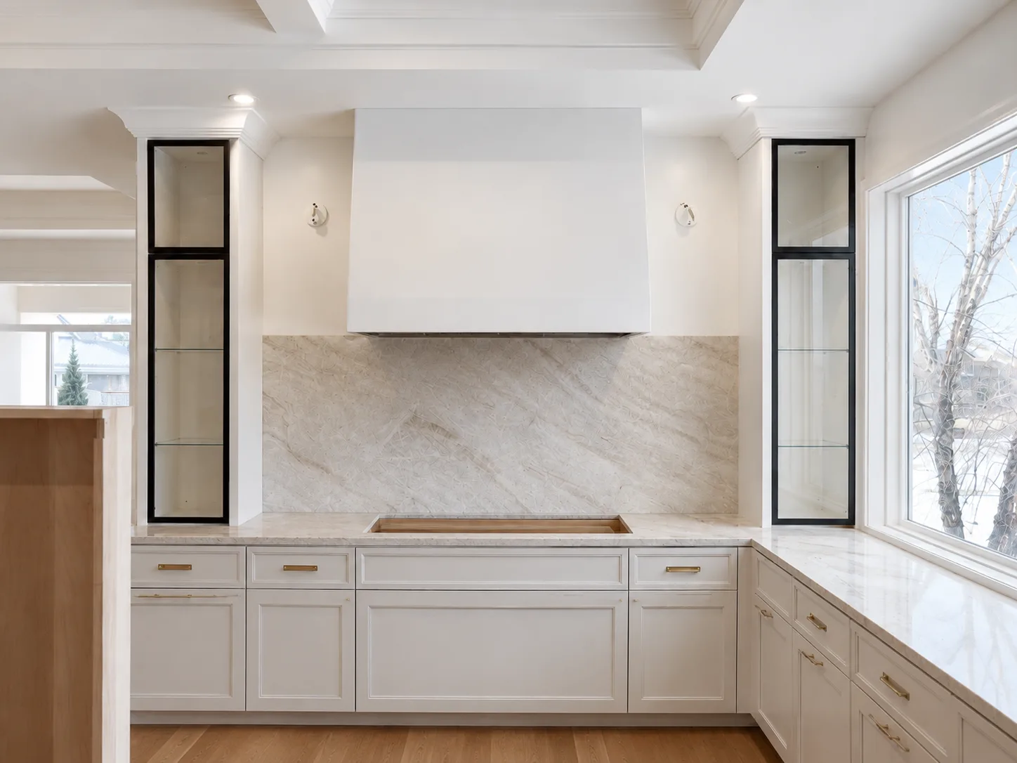 Subtle limewash finish on a centered oven hood surrounded by white cabinetry and black display towers